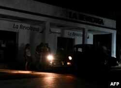 La gente usa un automóvil para iluminarse en una calle oscura durante un apagón en el municipio de Bauta, provincia de Artemisa, Cuba, el 18 de marzo de 2024. (Foto de YAMIL LAGE / AFP)